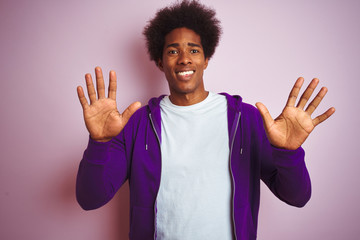 Young african american man wearing purple sweatshirt standing over isolated pink background showing and pointing up with fingers number ten while smiling confident and happy.