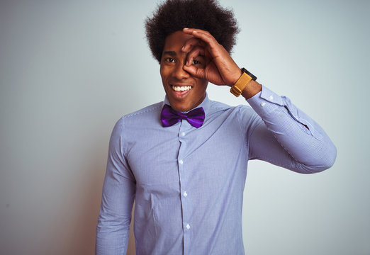 Afro business man wearing striped shirt and purple bow tie over isolated white background doing ok gesture with hand smiling, eye looking through fingers with happy face.