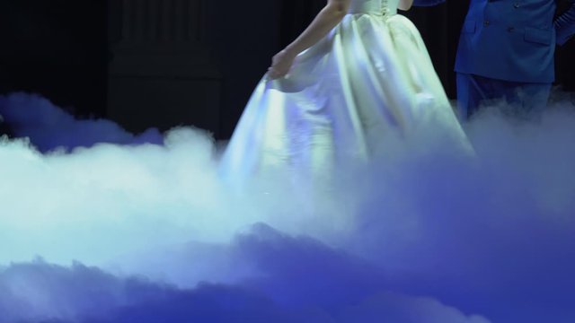 Handsome man - groom hold beautiful elegant bride in white wedding dress in thick puffs of blue fluffy smoke on the floor close up. First dance of wonderful loving couple in happy married day.
