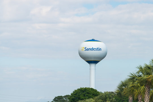 Miramar Beach, USA - April 24, 2018: Water tower against blue sky with palm trees and sign for Sandestin Golf Beach and Resort in Florida Panhandle, Pensacola island
