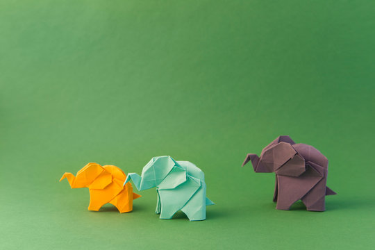 origami elephants made of colour paper on green background. paper and forest conservation concept. family and childhood. mockup, copy space
