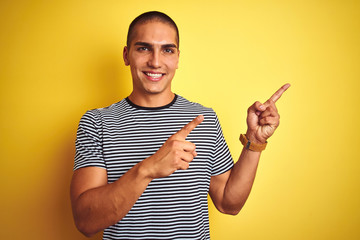 Young handsome man wearing striped t-shirt over yellow isolated background smiling and looking at the camera pointing with two hands and fingers to the side.