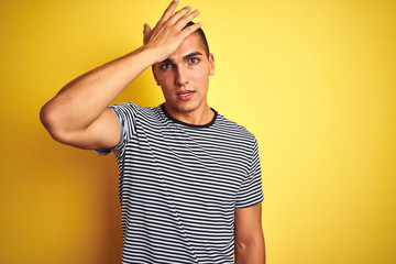 Young handsome man wearing striped t-shirt over yellow isolated background surprised with hand on head for mistake, remember error. Forgot, bad memory concept.