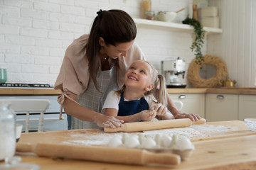 Preschool daughter enjoying helping smiling mother preparing homemade pastry.
