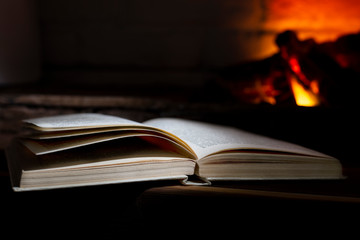 an open hardback book lies near a burning fireplace