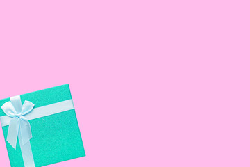 Green gift box with white ribbon isolated on pink background.
