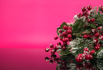 Close up of fake green leaves, red cherries isolated in pink background. Eve, Christmas New year concept.