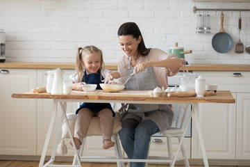 Happy young mother giving bans making class to daughter.