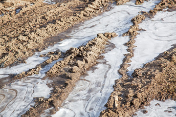 Dirty road with frozen puddles and traces outdoors.