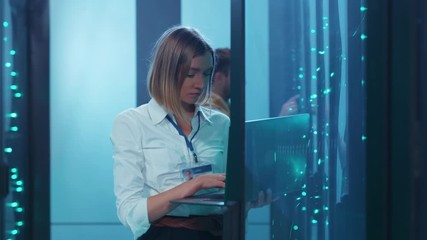 Young woman IT specialist opening rack server performing data center backups operations with laptop coworking in digital room. Cyber security.