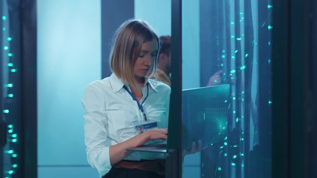 Young woman IT specialist opening rack server performing data center backups operations with laptop coworking in digital room. Cyber security.