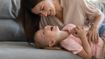 Smiling attractive brunette young mommy tickling daughter.