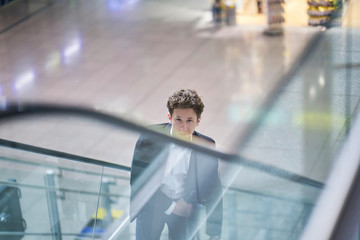 Young handsome smiling businessman inside the airport on an escalator with his rolling suitcase