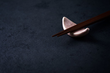Wooden chopsticks and chopstick rest on black paper background. Close up. Copy space. 
