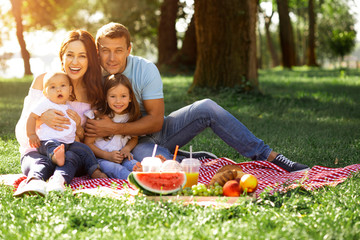 smiling parents embracing their kids and looking at the camera in the park