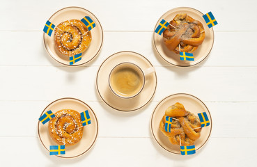 Swedish cinnamon buns (kanelbullar) and coffee on the white wooden table. Swedish flags. Coffee break (fika) concept. Top view.