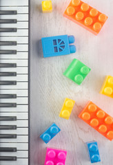  details of a children’s designer of different colors and shapes and a toy piano keyboard on a wooden tabletop. Flat lay