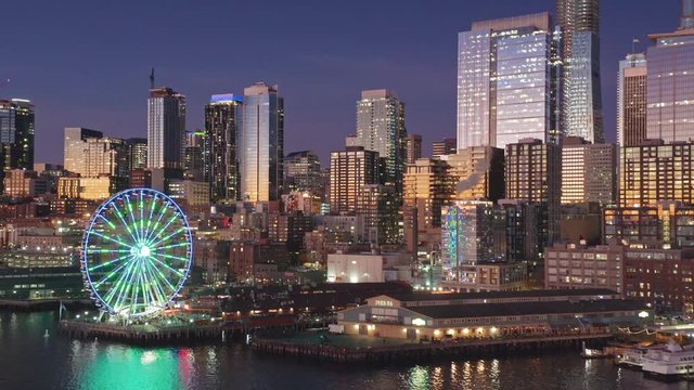 Aerial: Flying over the Seattle city skyline, Elliott Bay waterfront & Ferris wheel at sunset. Seattle, Washington, USA. 03 November 2019