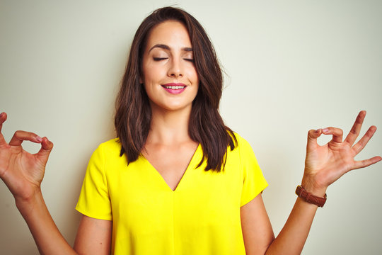Young beautiful woman wearing yellow t-shirt standing over white isolated background relax and smiling with eyes closed doing meditation gesture with fingers. Yoga concept.