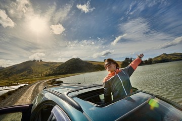Woman leaning out through the sunroof of a car on a countryside journey on Otago Peninsula, New Zealand