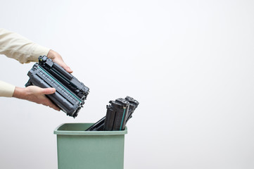 Male hands of an office worker stack spent cartridges in a bucket against a white wall.