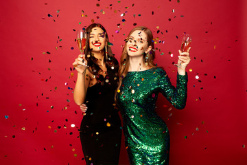  two beautiful models, a redhead and a brunette in New Year's dresses, having fun and smiling with...