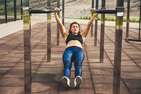 girl trains outdoors in street gym. Training of biceps and triceps. woman parallel bars workout exercise. female athlete exercising on parallel bars, doing push-ups. Sport and bodybuilding concept