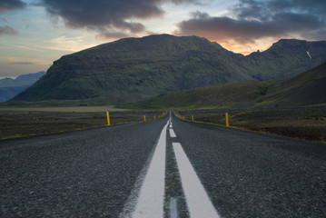 Sunset and vivid colors over big mountain scenery at the end of a long road. Road trip and landscape concept.