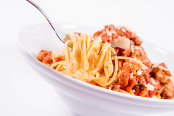Spaghetti bolognese being eaten with a fork on a white background