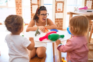 Beautiful teacher woman and toddlers playing around lots of toys at kindergarten