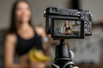 Asian woman making video for her blog on healthy eating using tripod mounted digital camera