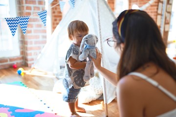 Beautiful teacher and toddler playing with elephant doll around lots of toys at kindergarten