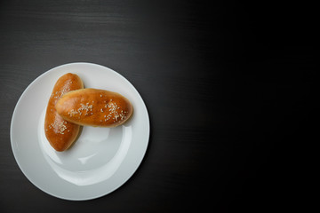 Delicious sesame buns or pies on white plate standing on black wooden table background. Tasty unhealthy snack for lunch or breakfast. Overweight, diet, nutrition, eating habits concept. Place for text