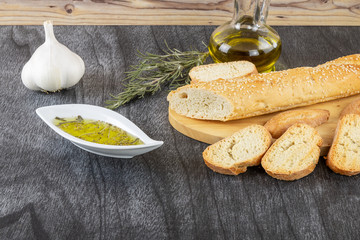 Baguette and olive oil dipping. Delicious Greek snack food and drink. Olive oil with herbs and garlic. Bread olive oil sauce on wooden background.