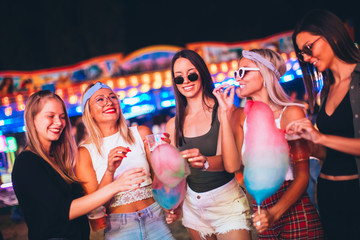 Female friends eating cotton candy and drinking beer in amusement park