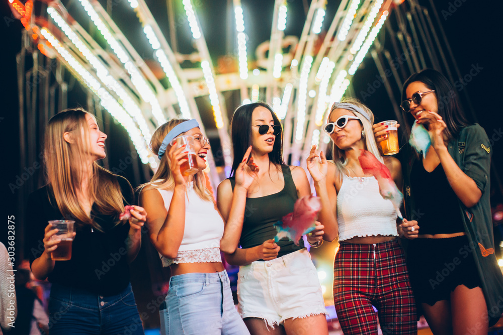 Wall mural female friends eating cotton candy and drinking beer in amusement park