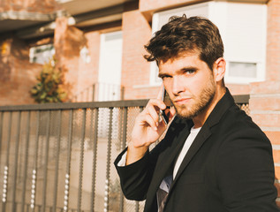 Close-up of attractive young man with beard in suit speaks on the phone looking at camera