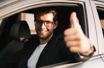 Attractive young man with a beard and glasses smiles and says ok with his hand while looking out...