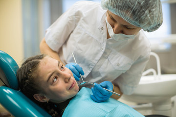 Female dentist doing teeth checkup of little girl looking with fear sitting in a dental chair in medical clinic.