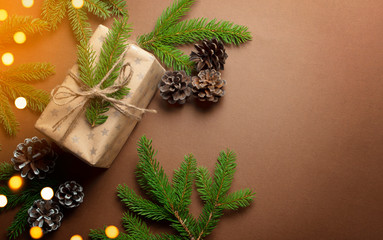 Merry Christmas and happy New Year concept with gift box, branches, pine and fairy light on brown background. Top view