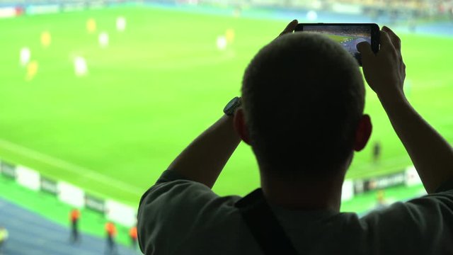 Male sports fan filming football soccer game on smartphone, excited supporter. Sports fan enjoying match