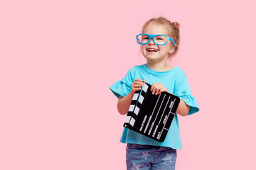 Funny smiling child girl in cinema glasses hold film making clapperboard isolated on pink background. Studio portrait. Childhood lifestyle concept. Copy space for text. - obrazy, fototapety, plakaty