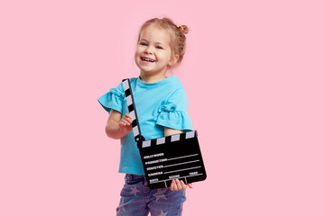 Funny smiling child girl in cinema glasses hold film making clapperboard isolated on pink background. Studio portrait. Childhood lifestyle concept. Copy space for text.