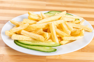 French fries, on a plate, with a cucumber.