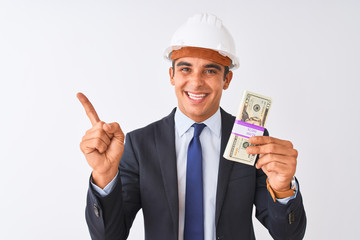 Young handsome architect man wearing helmet holding dollars over isolated white background very happy pointing with hand and finger to the side