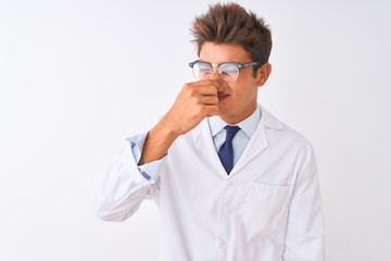 Young handsome sciencist man wearing glasses and coat over isolated white background smelling something stinky and disgusting, intolerable smell, holding breath with fingers on nose. Bad smells 
