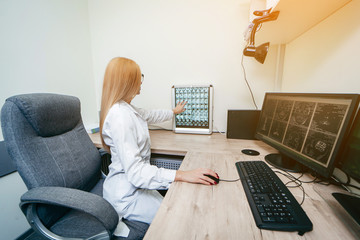 Young blonde doctor typing on computer and examine MRI picture