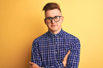 Young handsome man wearing casual shirt and glasses over isolated yellow background skeptic and nervous, disapproving expression on face with crossed arms. Negative person.