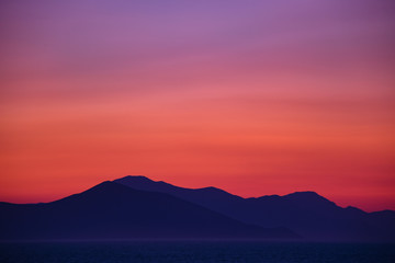 Beautiful colorful sunset seen from the island surrounded with sea over the high mainland hills 