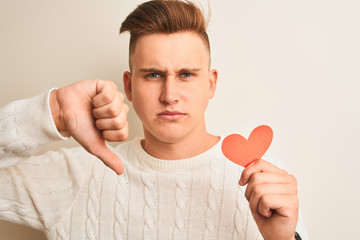 Young handsome romantic man holding paper hearts standing over isolated white background with angry...